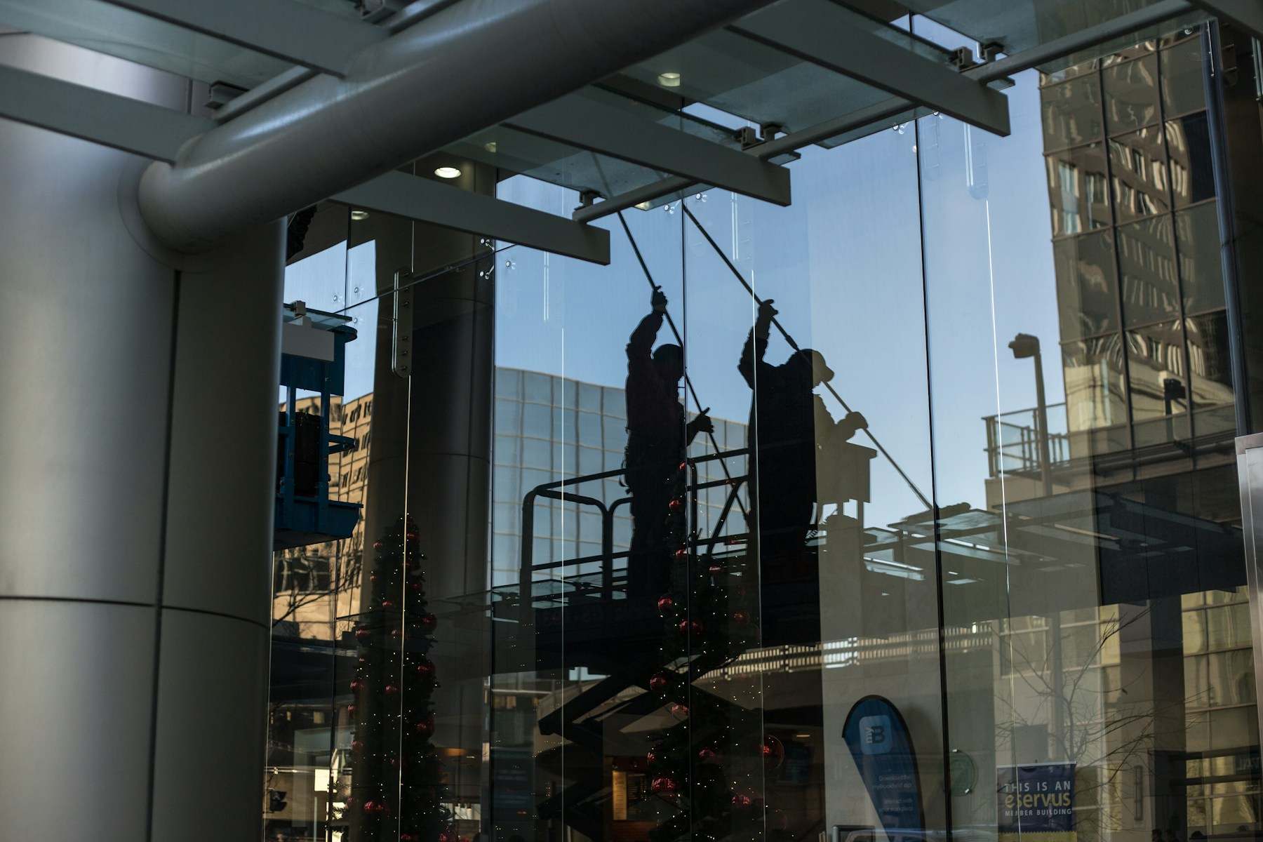 Zwei Glasreiniger auf einer Hebebühne hinter einer großen Glasfassade, als Silhouetten