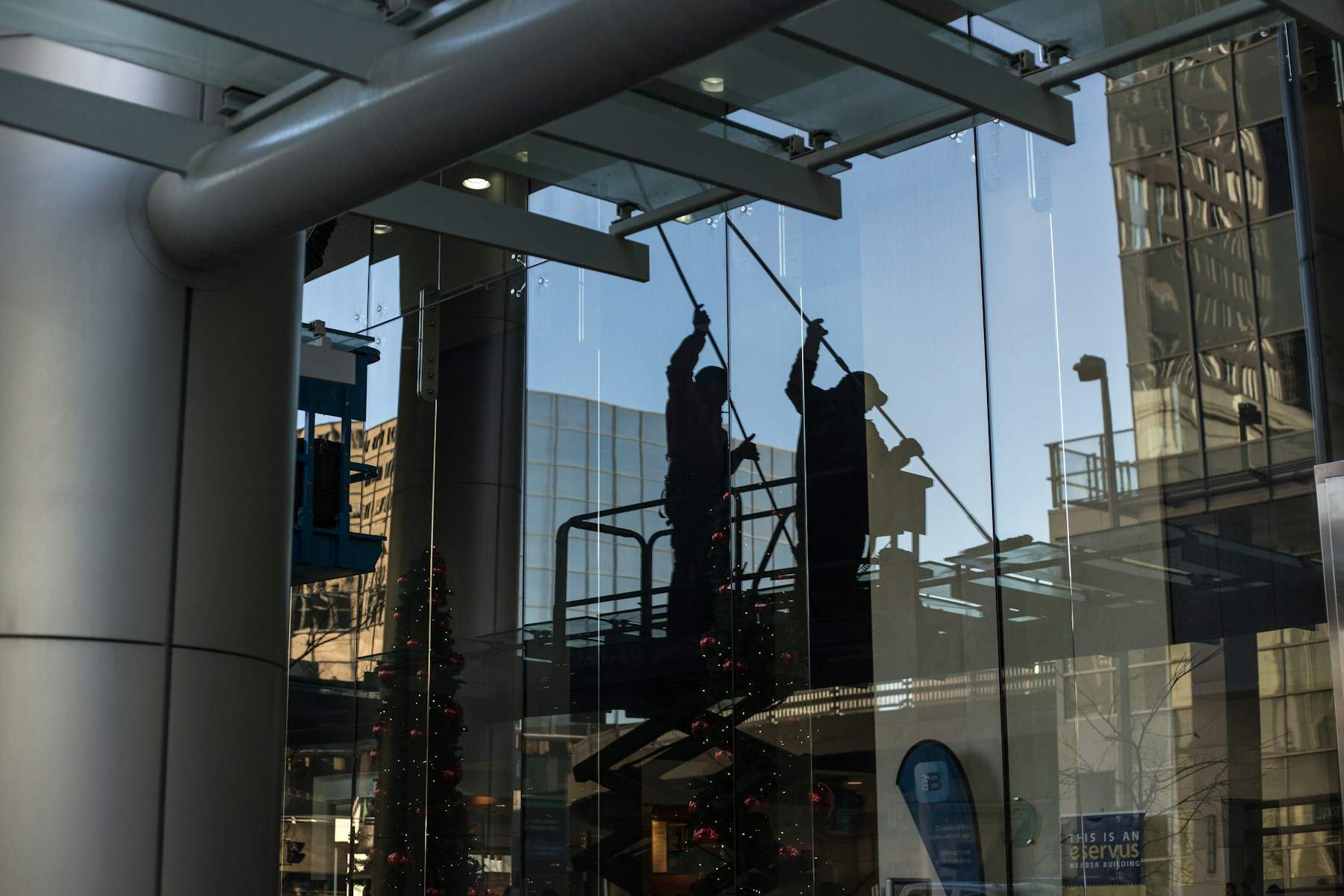 Zwei Glasreiniger auf einer Hebebühne hinter einer großen Glasfassade, als Silhouetten